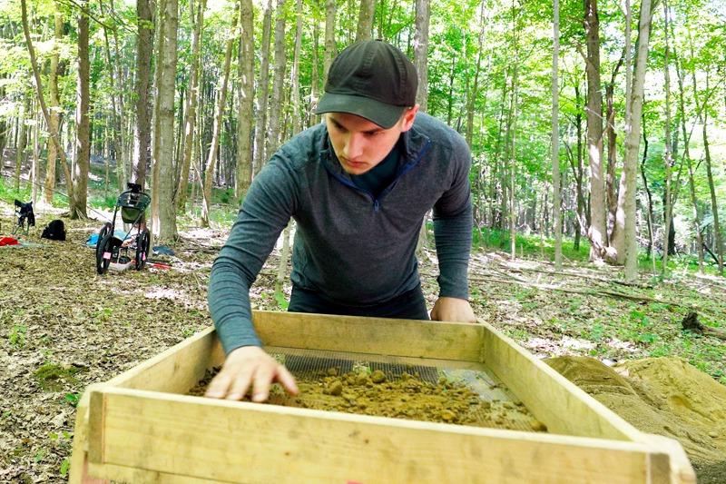 A college student works at an archaeology dig in the woods