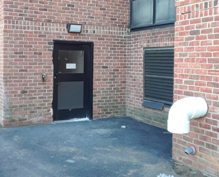 Back entrance of brick building with metal black door next to exhaust pipe for the natural gas heat exhaust 